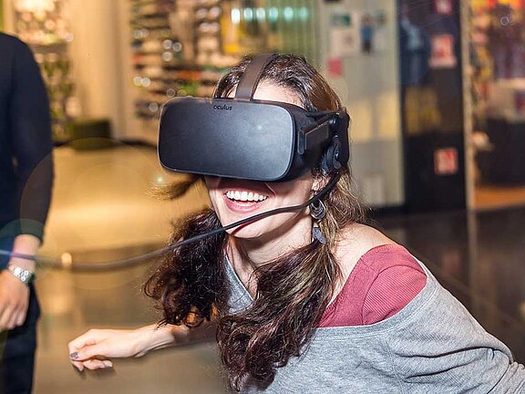 Eine Frau trägt eine schwarze Simulationsbrille und lacht dabei