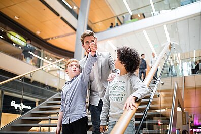 Ein Erwachsener und zwei Kinder auf den Treppen eines Shopping-Centers