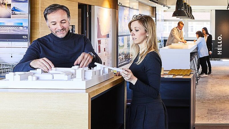 Im Vorder- sowie im Hintergrund stehen Personen vor einem Architekturmodell