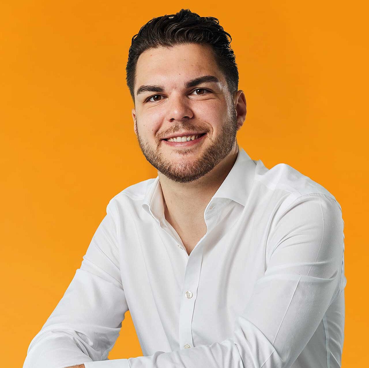 Auf dem Bild ist das Portrait eines jungen Mannes zu sehen, vor einem orangem Hintergrund