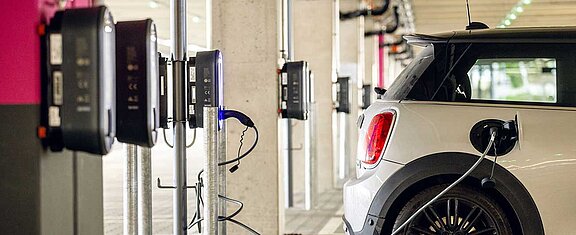 Ein E-Auto steht auf einem Parkplatz und ist an einer Ladestation angeschlossen