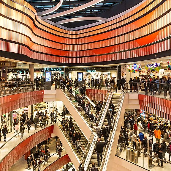 Im Inneren eines Shopping-Centers mit imposanter roter Deckenbeleuchtung und vielen Besucherinnen und Besuchern in den Kaufhaus-Gängen