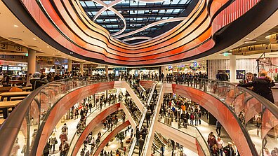 Im Inneren eines Shopping-Centers mit imposanter roter Deckenbeleuchtung und vielen Besucherinnen und Besuchern in den Kaufhaus-Gängen