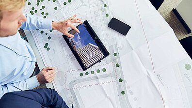 Eine Person sitzt vor einem Projektplan und arbeitet an einem Tablet