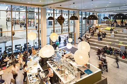 Der Eingangsbereich des Marstalls mit einer Kaffee-Bar und Besuchern, die auf einer Treppe sitzen.