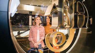 Zwei Shopping-Center-Besucherinnen schauen sich etwas in einem Schaufenster an