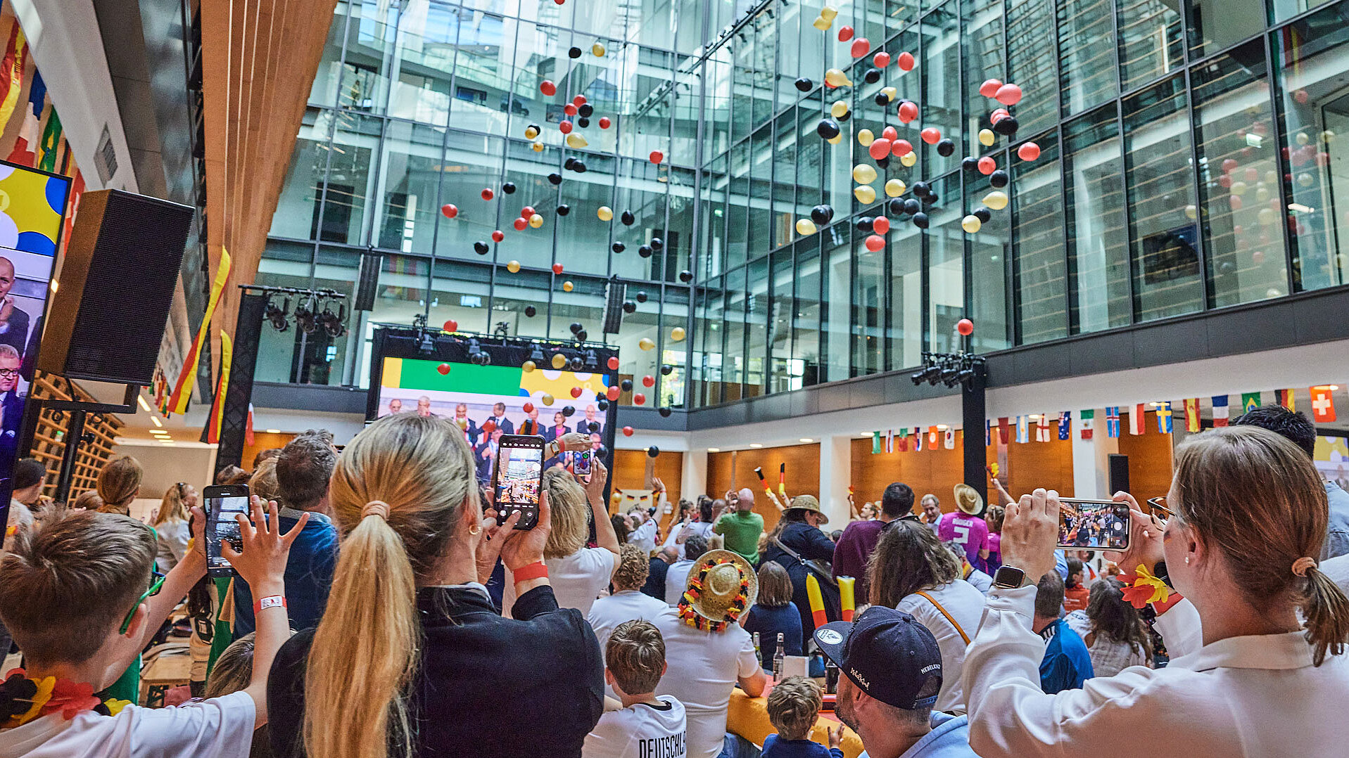 Viele Menschen stehen im Atrium der ECE und schauen ein Fußballspiel, in der Luft sind schwarze, rote und goldene Ballons.
