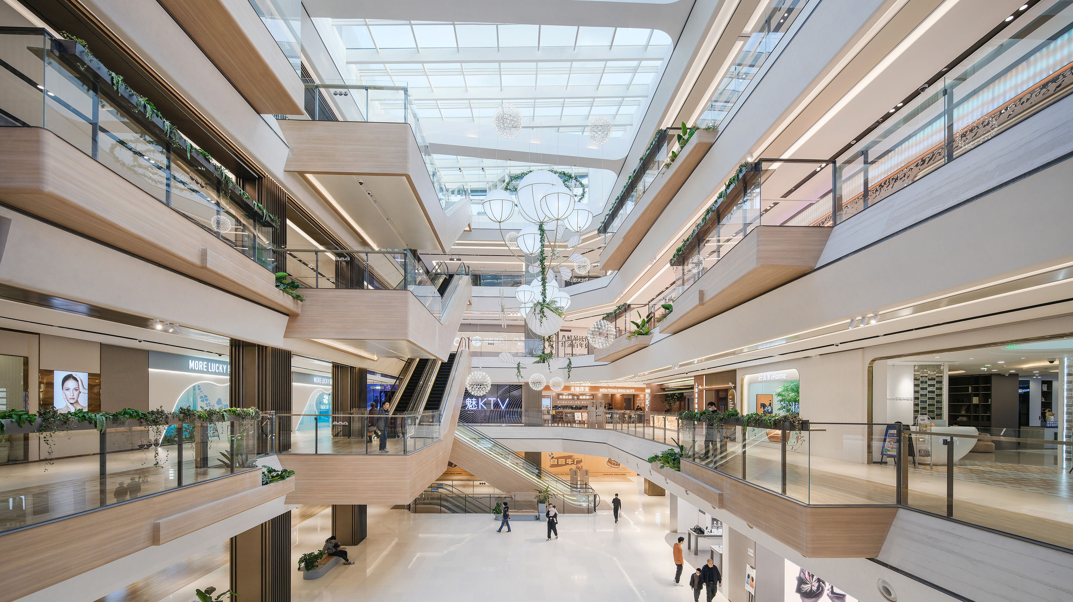 View inside a brightly coloured shopping centre with special architectural features, light wood panelling and sunlight streaming through the glass roof.
