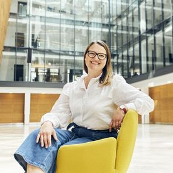 Eine Frau sitzt auf einem gelben Sessel. Im Hintergrund ist das ECE-Bürogebäude zu sehen.