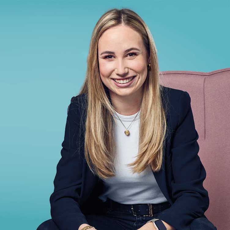 Auf dem Bild ist unsere Kollegin Norina Bartling zu sehen. Sie sitzt vor einem türkisem Hintergrund.