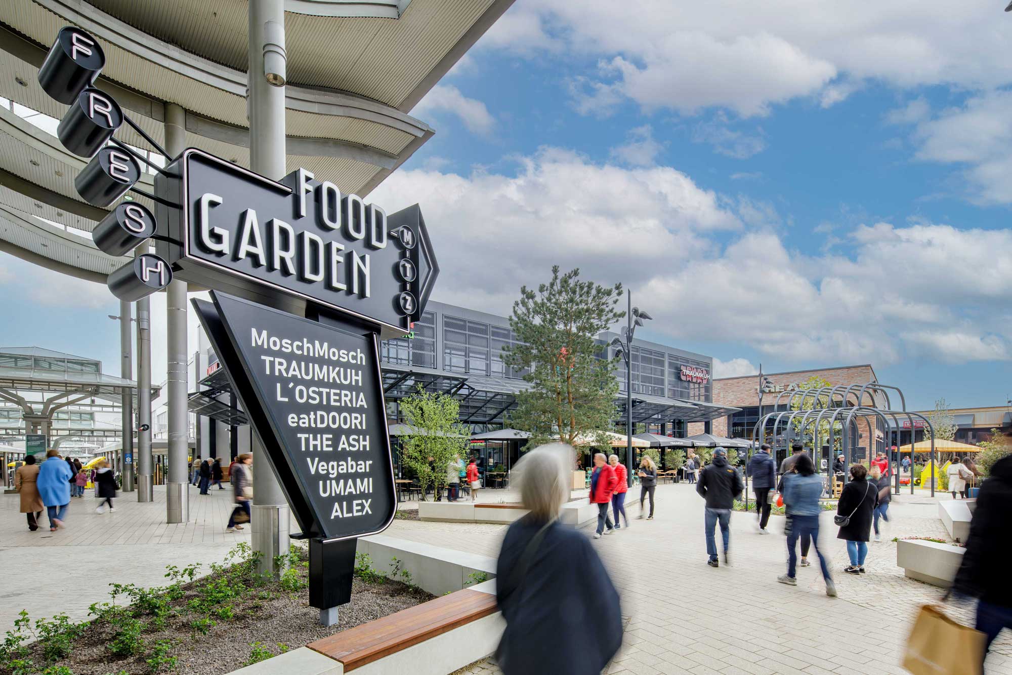 Auf dem Bild ist ein Totempfahl mit der Aufschrift "Food Garden" zu sehen, dahinter stehen Gebäude.