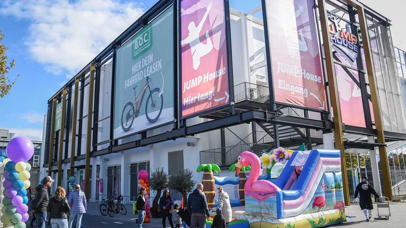 Es ist ein Gebäude mit bunten Fahnen zu sehen, darauf steht Werbung für B.O.C. und JumpHouse 